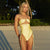 Woman in a yellow swimsuit standing on a beach with palm trees in the background