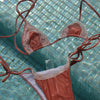 Bikini set with coral-colored top and white bottom on a tiled pool floor.