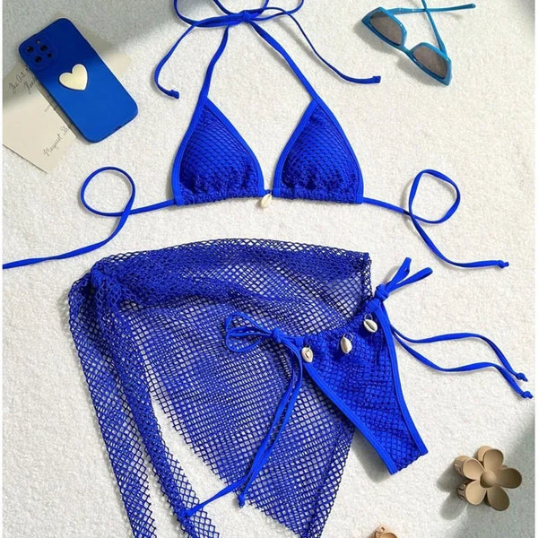 Blue bikini set on a white surface with a phone, sunglasses, and flowers.