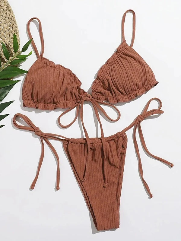 Brown bikini set on a white background with a straw hat and green leaves.