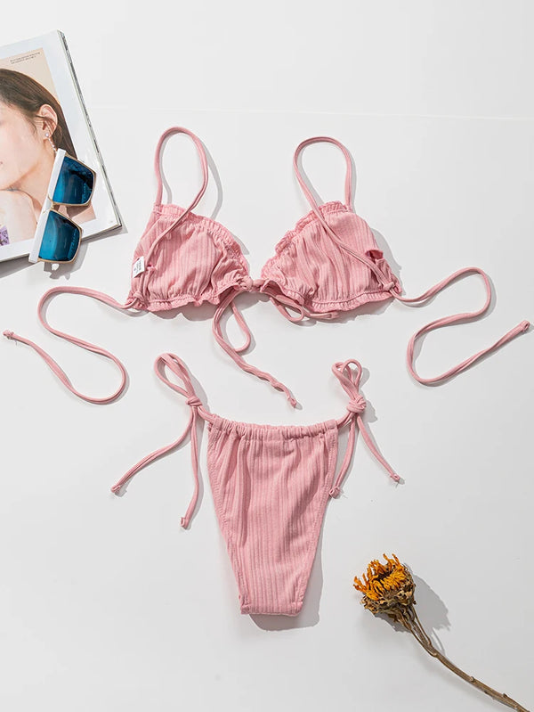 Pink bikini set on a white surface with a magazine and sunglasses.