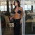 Woman in a black bikini holding a Louis Vuitton bag in an indoor setting with tables and chairs.