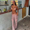 Woman in pink bikini and lace pants standing by a counter with a tropical setting.