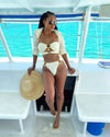 Woman in a white bikini and cover-up on a boat with turquoise water in the background