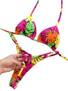 Colorful bikini set with leaf patterns held by a hand against a light background