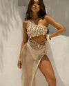 Woman wearing a one-shoulder embellished top and fishnet skirt against a neutral background