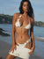 Woman in a white bikini and skirt on a beach with ocean and sky in the background