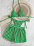 Green and white striped bikini set on a marble surface with decorative plates.