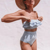 Woman wearing a blue and white striped bikini with a straw hat on a light background
